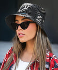 Fresh Unisex Black Bucket Hat With Dope Graphic Print And Super Lightweight Breathable Polyester Twill Fabric Easy Foldable Sun Hat For Chill Outdoor Vibes worn with sunglasses.