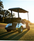 Black golf cart on a green field at sunset showcasing the back view and roof structure.