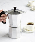 Person using Stovetop Moka Pot Espresso Maker For Home Brew 6 Cup Greca Style Coffee Pot For Italian And Cuban Cafe Perfect For Lattes Cappuccinos Americanos Quick Rich Brews In Silver on a countertop
