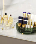 Glass perfume organizer with gold accents on a marble shelf, next to a green organizer with cosmetic bottles.