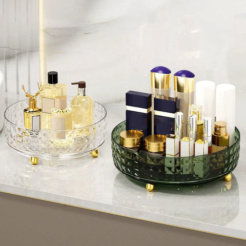 Glass perfume organizer with gold accents on a marble shelf, next to a green organizer with cosmetic bottles.