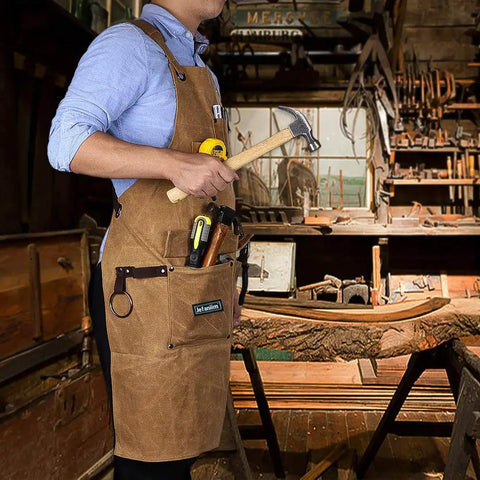 Person wearing Heavy Duty Waxed Canvas Apron For Woodworking With Pockets And Cross Back Straps, holding tools in workshop.