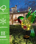 Outdoor Solar Hummingbird Garden Lights For Pathway And Patio metal stake light in rain, green and yellow LED glow, evening.
