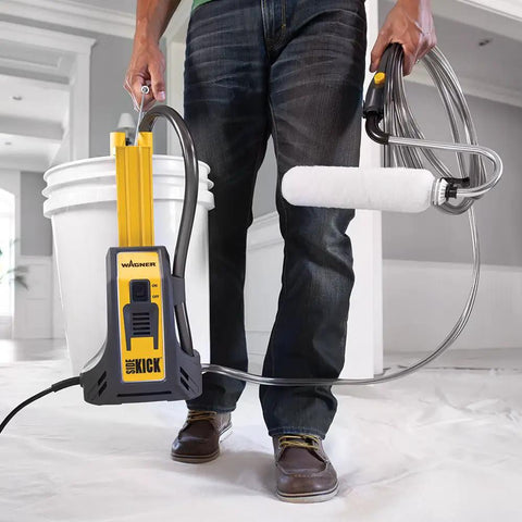 Man holding Smart Sidekick Workhorse Power Paint Roller Direct Feed System, roller pulling paint from 5-gallon bucket, in large room.