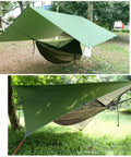 Oversized Waterproof Rain Fly Camping Hammock With Mosquito Net And Tree Straps Carabiners Poles And Gear For Backpacking Hiking And Backyard Use Army Green set up in a park with trees.