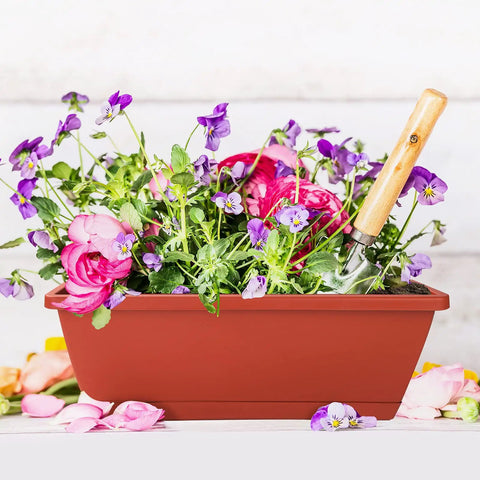Red 17-inch rectangular plastic window box planter with purple and pink flowers and a gardening tool visible on top.