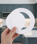 Hand holding No Fuss Peel And Stick White Round Plumbing Access Panel With Super Secure Grip Removable Abs Pipe Hole Cover For Ceiling And Drywall Six Inch No Drill Quick Swap.