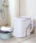 Hand Crank Washing Machine With Biomimetic Scrub Interior Manual Portable Laundry Soaker placed beside a basin of clothes in a bathroom.