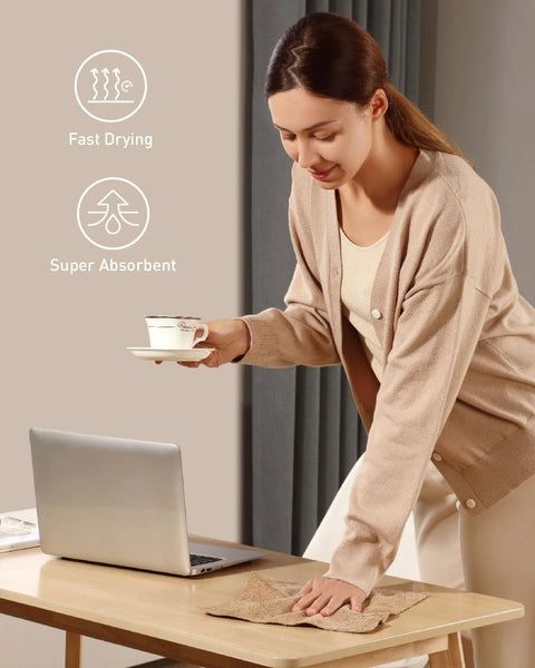 Fantasticlean tan microfiber cleaning cloth being used to wipe a desk beside a laptop (front view).