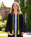 Graduate wearing black gown and 67 Inch Gold Graduation Honor Cord With Tassels, holding diploma, standing outside a brick building.