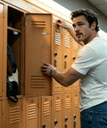 Person opening school locker in hallway, wearing casual white t-shirt and jeans, looking at camera