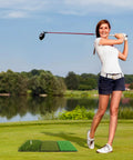 Woman practicing swing on 3-In-1 Golf Practice Mat With Realistic Turf Surfaces next to a scenic lake.