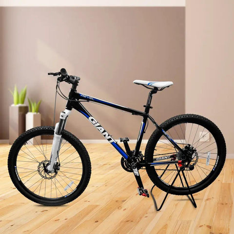 Mountain bike on adjustable folding bike stand on wooden floor, showcasing the adjustable folding bike stand for 20 to 29 inch bikes floor mounted alloy steel rack that keeps your ride scratch free great for indoor garage storage and quick repairs.