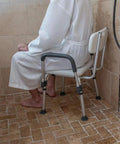 Person sitting on adjustable white bath and shower chair with depth adjustable back, 300 lb capacity, senior safe shower seat.