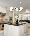 Six Light Sputnik Chandelier In Matte Black With Globe Glass Shades hanging over kitchen island in modern dining area.