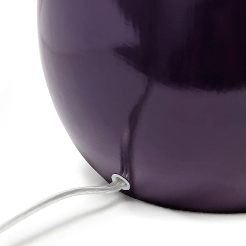 Close-up of the curved eggplant purple ceramic base of the table lamp with visible cord.