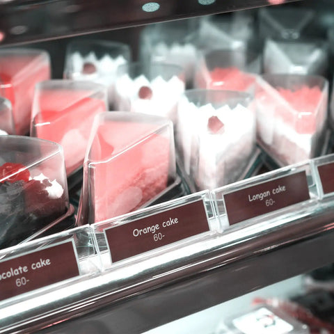 Slices of cake in a refrigerated display case including orange, longan, and chocolate varieties.
