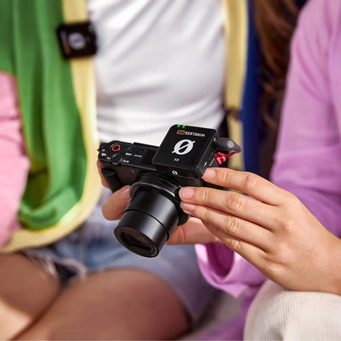 Person holding a camera with Plug-And-Play Ultra Compact Wireless Microphone System With Built-In Mics, GainAssist Technology, and 100m Range.