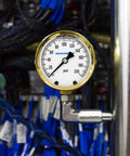 Built Tough Heavy Duty Fully Brass Hydraulic Glycerin Filled Pressure Gauge With Two And A Half Inch Dial Quarter Inch NPT Lower Mount 0 To 200 Psi And KPa For Measuring Non Corrosive Gas And Liquid Pressure In Industrial And Home Setups mounted on a pipe with cables in the background