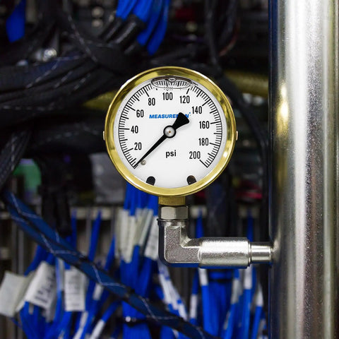 Built Tough Heavy Duty Fully Brass Hydraulic Glycerin Filled Pressure Gauge With Two And A Half Inch Dial Quarter Inch NPT Lower Mount 0 To 200 Psi And KPa For Measuring Non Corrosive Gas And Liquid Pressure In Industrial And Home Setups mounted on a pipe with cables in the background