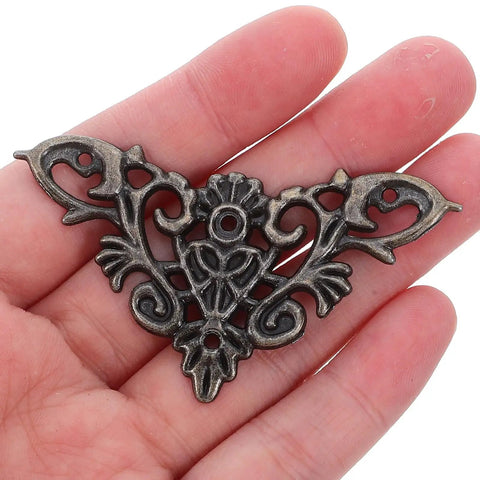 Person holding a piece from the Eight Piece Jewelry Box Corner Protectors Set, Vintage Zinc Alloy Triangle Edge Guards With Easy Installation
