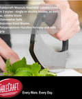TableCraft H6610 single mezzaluna with stainless steel blade and black handle cutting fresh mint leaves.