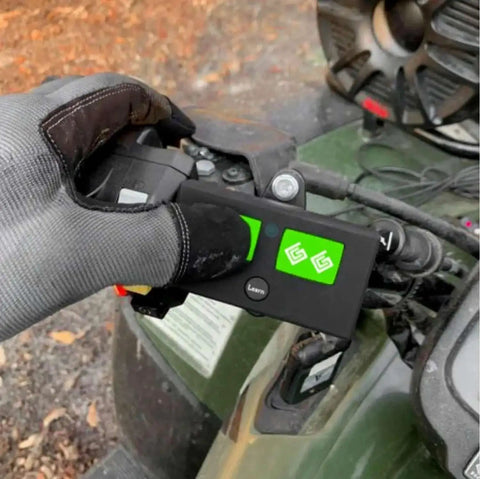 Gloved hand holding AXR1 Water-Resistant 3-Button Remote For Automatic Gate Openers on an ATV dashboard