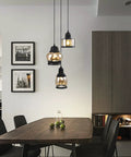 Three Light Modern Glass Pendant Chandelier for Dining Room and Kitchen Island with Amber Glass Shades hanging over table.