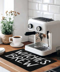Spooktacular Black Witches Brew Coffee Station Mat Featuring Quick Dry Absorbent PU Material Designed For Kitchen Counter Espresso Machine Setup 28 By 18 Inch Halloween Spill Proof Drip Catch Pad on kitchen countertop.