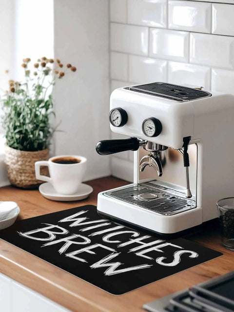 Spooktacular Black Witches Brew Coffee Station Mat Featuring Quick Dry Absorbent PU Material Designed For Kitchen Counter Espresso Machine Setup 28 By 18 Inch Halloween Spill Proof Drip Catch Pad on kitchen countertop.