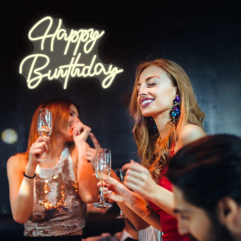 People celebrating at a party under 'Happy Birthday' neon sign, showcasing Smile Face Neon Sign Birthday Light 13 By 13 Inches Portable USB Powered Warm White Glow For Parties Take Anywhere Easy To Install With 2 Meter USB Cable Photo Backdrop And Party Ready Decor For Events.