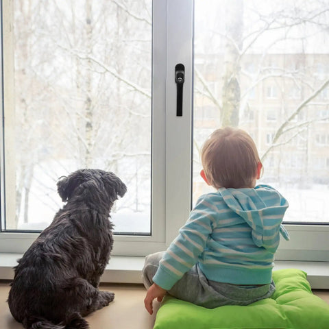 Child and dog sitting by a window with a snowy view, visible window handle with lock for security and easy use.