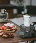 Portable 3-in-1 Butane Camping Heater With 3750 BTU Firepower on a wooden table next to a white coffee maker and food platters.