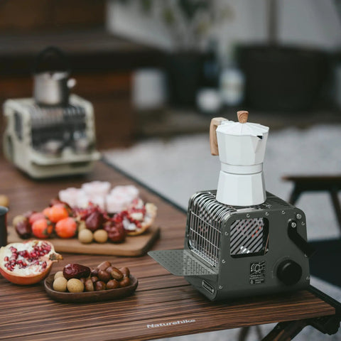 Portable 3-in-1 Butane Camping Heater With 3750 BTU Firepower on a wooden table next to a white coffee maker and food platters.
