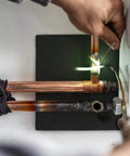 Person welding copper pipes with heat shield protecting the surface, demonstrating use of 9x12 Inch Heavy Duty Heat Shield Barrier Blanket.