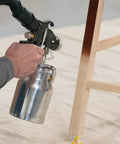 User holding stainless steel container of Stationary Hvlp Finishing Sprayer For Woodworkers Wanting Killer Results On Furniture Restoration Projects Using Pro Grade Metal Spray Gun For Super Smooth Ultra Fine Coating Every Time.