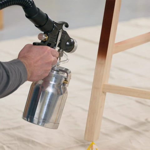 User holding stainless steel container of Stationary Hvlp Finishing Sprayer For Woodworkers Wanting Killer Results On Furniture Restoration Projects Using Pro Grade Metal Spray Gun For Super Smooth Ultra Fine Coating Every Time.