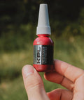Person holding a 10ml tube of blue thread locker for knife and gun pivot screws, oil tolerant and fast curing, in an outdoor setting.