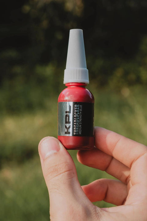 Person holding a 10ml tube of blue thread locker for knife and gun pivot screws, oil tolerant and fast curing, in an outdoor setting.
