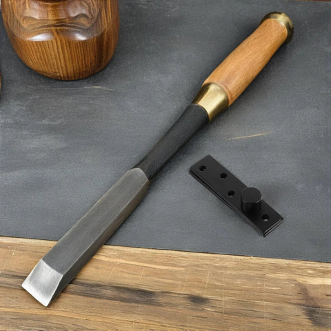 Wood chisel with wooden handle on a workshop table next to a black metal hinge.