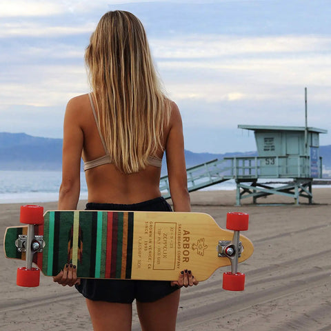 Person holding a skateboard with colorful stripes near a beach.
