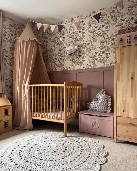 Kids Bed Canopy With Ruffles In Pastel Nougat hanging over a baby crib in a nursery with floral wallpaper and bunting.