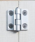 Installed torque position control hinge, aluminum alloy, white finish, mounted on light wood boards.