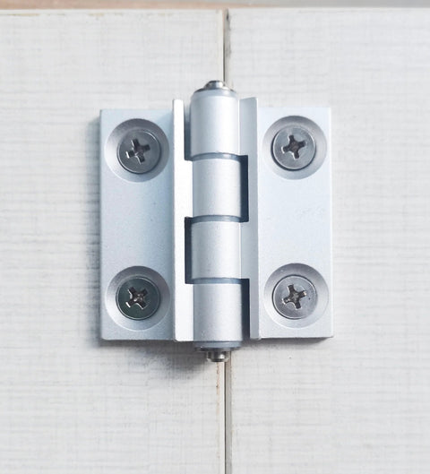 Installed torque position control hinge, aluminum alloy, white finish, mounted on light wood boards.