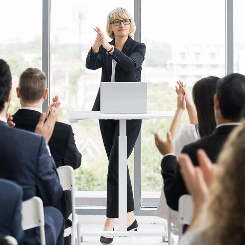 Woman standing at a podium using Go To Mobile Rolling Laptop Desk With Two Lockable Wheels Height Adjustable Sit Stand Computer Workstation.