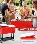 80QT Rolling Cooler On Wheels With Bottle Opener Outdoor Beverage Cooler For Patio And Backyard BBQ Beach Trip Or Party Holds Up To 100 Cans Keeps Drinks Cold 48 Hours And Warm 8 Hours Easy Access Storage Tray shown in red with open lid, party setting in background.