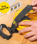 Close-up of a hand using Wrap-It Storage Straps 17-Inch 2-Pack Heavy-Duty Hook And Loop Cord Carrier with handle on yellow cord.