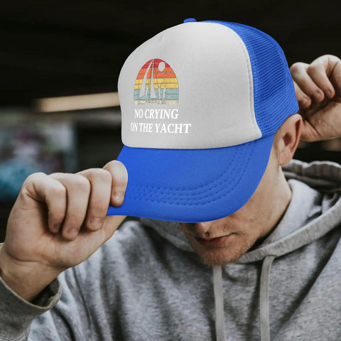 Man wearing a blue and white trucker hat with 'No Crying on the Yacht' text, adjusting brim, casual hoodie outfit