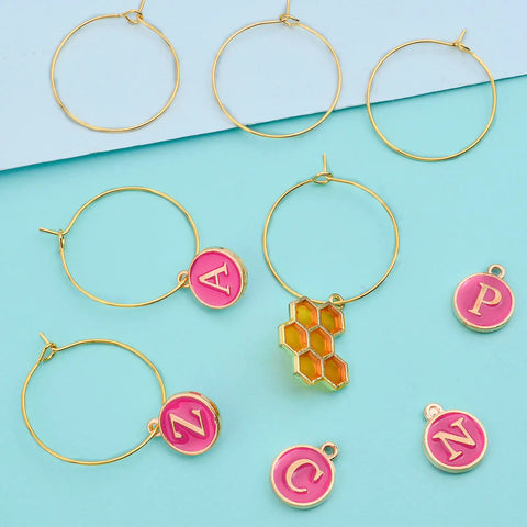 Rose Red Enamel Alphabet Charms And Golden Wine Glass Marker Rings Set on a blue background with colorful charms visible