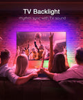 Four people watching TV with vibrant RGB lights from 150Ft LED Strip Lights Kit With App Control And IR Remote, music sync feature.